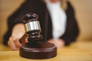 Hand holding a gavel, poised to strike on the sounding block in a courtroom setting.