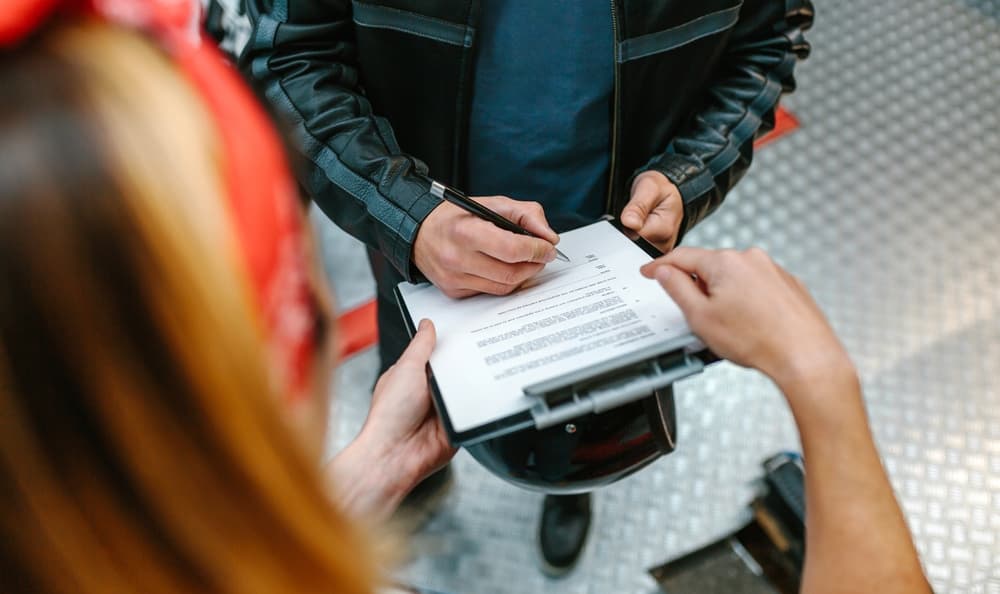 Person signing a document on a clipboard held by another, likely discussing financial settlement agreements.