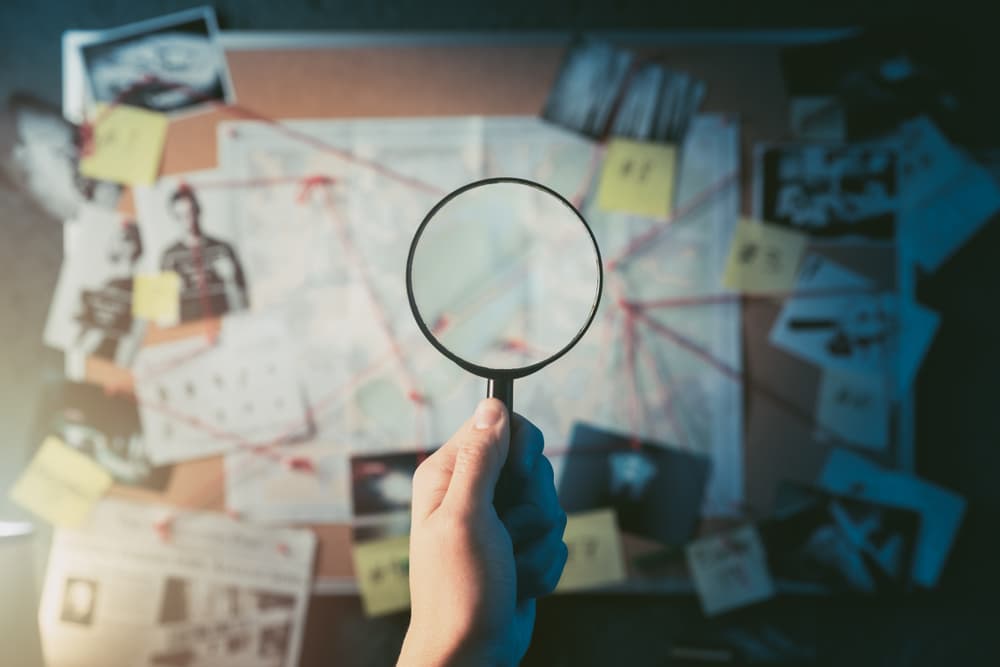 Investigator examining evidence board with magnifying glass, revealing crime scene details through photos and map.