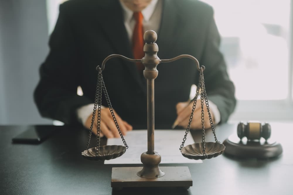 Legal professionals in office, deliberating contract papers with a brass scale on the desk. Image conveys concepts of law, legal services, advice, and justice, with a film grain effect.