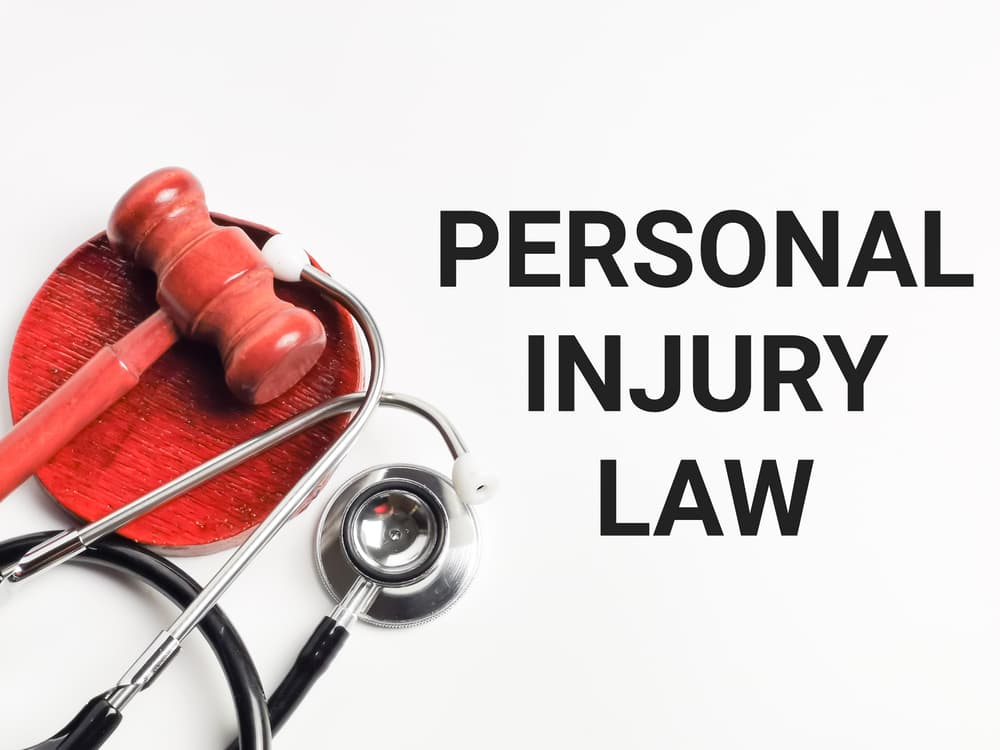 Close-up view of a white background with the phrase PERSONAL INJURY LAW, accompanied by a gavel and stethoscope in selective focus.