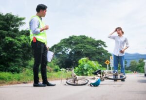 Outdoor collision scene involving a car and a bicycle, with people including an insurance officer and a young girl or cyclist.