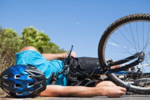Bicyclist injured on sunny day after road accident, lying on pavement.