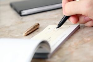 Man's hand writing a cheque on a table with pen and chequebook