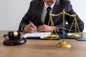 A legal professional works on documents and reports for an important case, with a gavel and scale on the table in a courtroom.