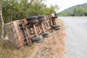 A large overturned truck on the side of a road. The truck is on its left side, and the trailer appears to be damaged. 