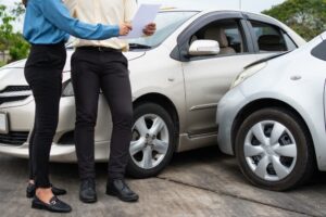 Drivers exchanging contact information and insurance details via smartphones after a car accident for insurance claims.