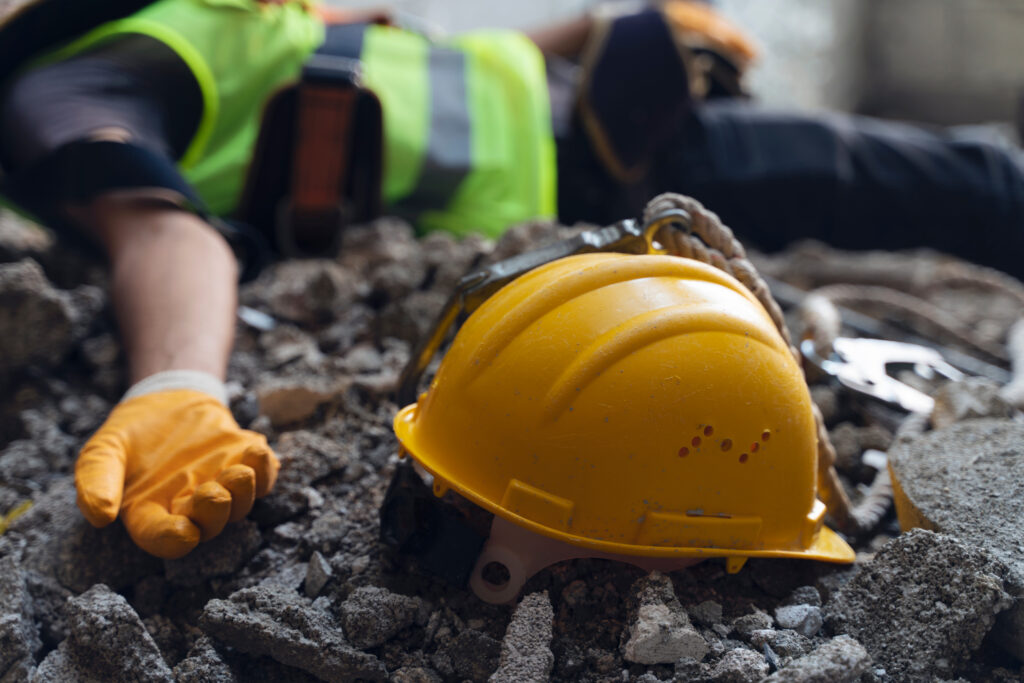 Construction worker injured on site with safety helmet on rubble after workplace accident.