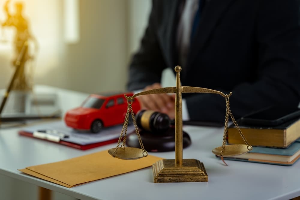 Scales of justice, red toy car, and gavel on a desk symbolizing guidance from a car accident lawyer
