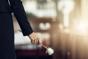 Hand holding a rose at a funeral ceremony, symbolizing grief and mourning amidst floral arrangements in a chapel or cemetery.