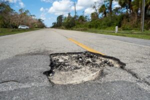 Cracked American road with deep potholes, urgently needing repair.