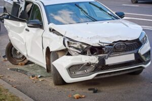 Severely damaged car with broken headlights after a road incident. Front-end and rear-end collision aftermath showing extensive destruction from a high-impact traffic accident.