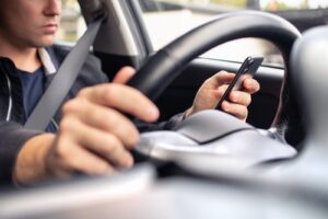 Man driving a car while looking at a smartphone.