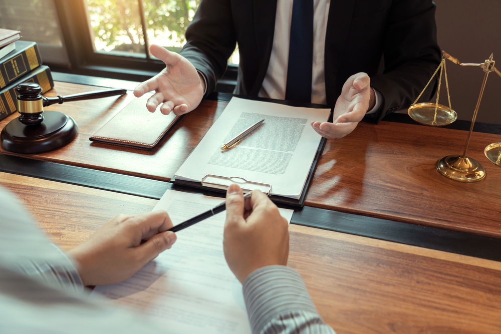 Attorney consulting with client over legal documents at a law office desk with gavel and scales of justice