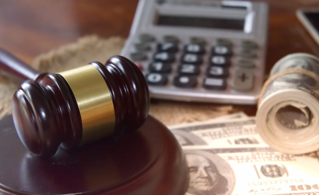 Judge’s gavel with money, calculator, and rolled cash symbolizing legal fees and financial settlements.