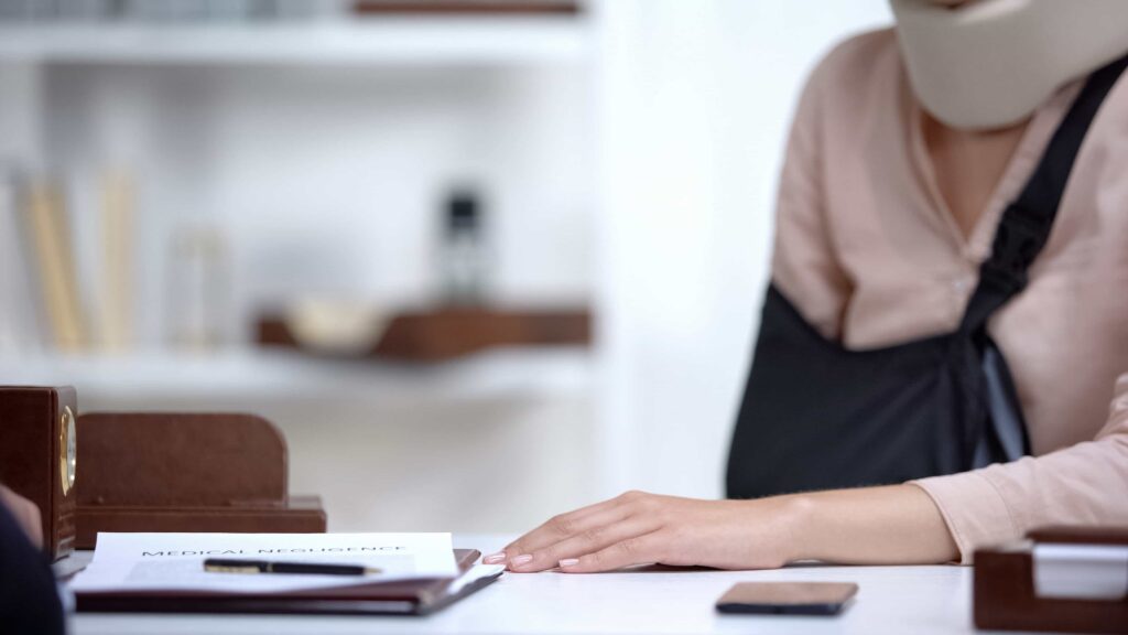 Injured woman with neck brace and arm sling filing medical negligence claim with lawyer.