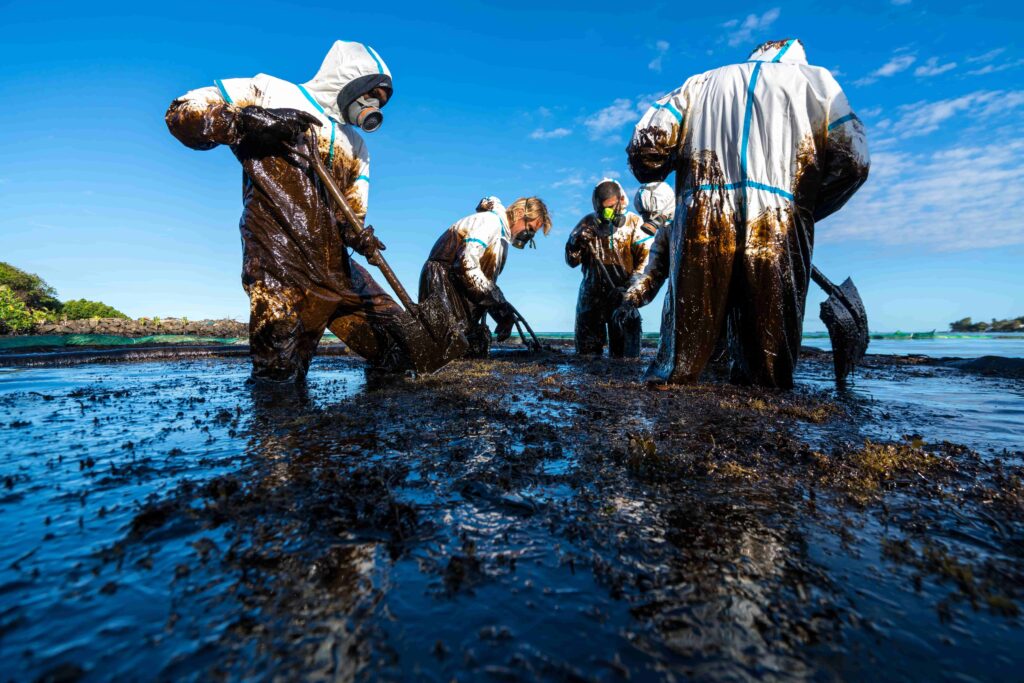 Environmental workers in protective suits cleaning oil spill on beach with shovels to restore polluted coastline.