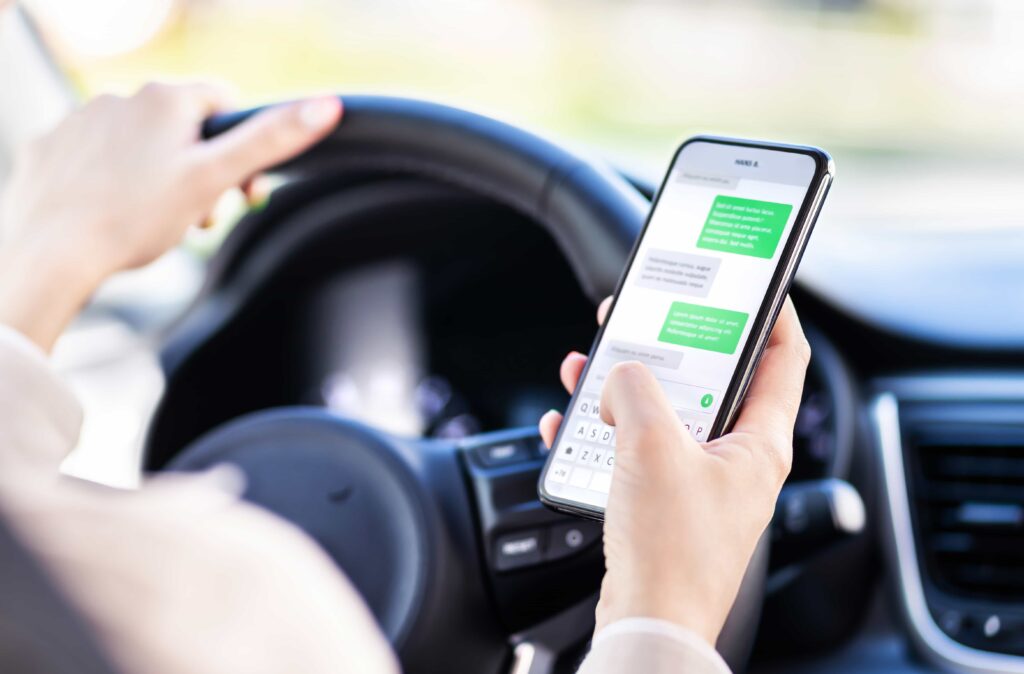 Driver texting on smartphone while driving, showing the dangers of distracted driving and cell phone use behind the wheel.