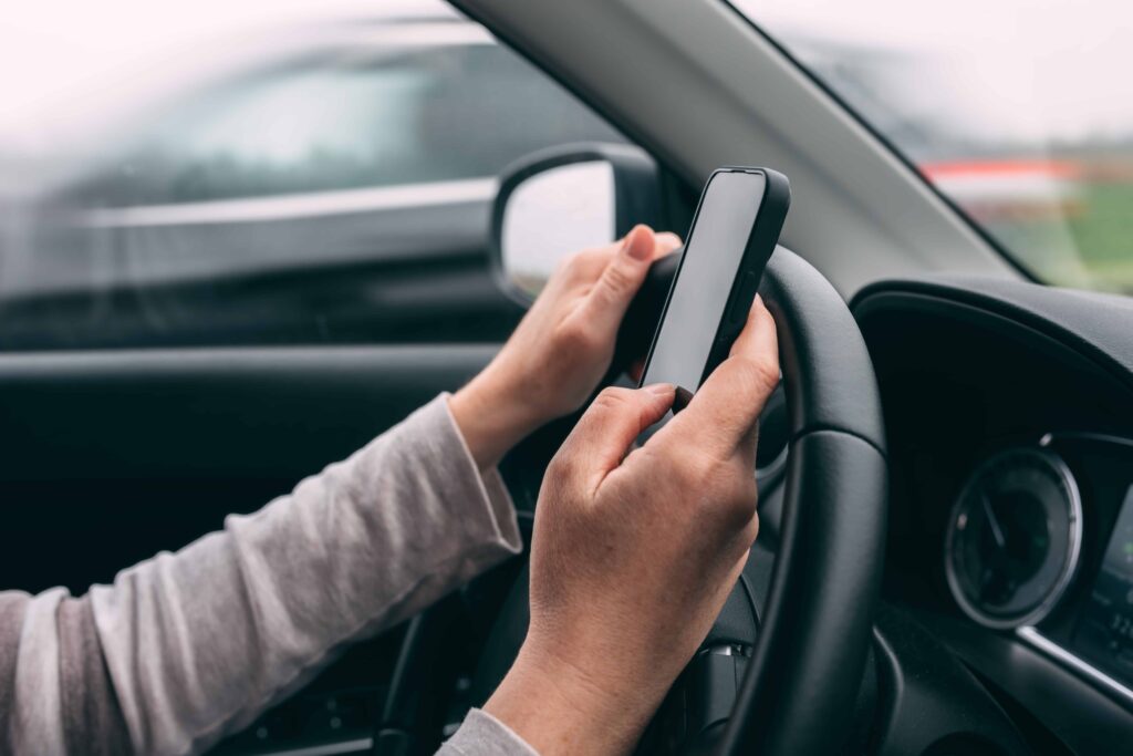 Driver using a smartphone behind the wheel, illustrating distracted driving and texting while driving danger.
