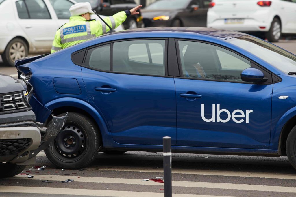 Uber car accident with rear-end damage being inspected by police officer.