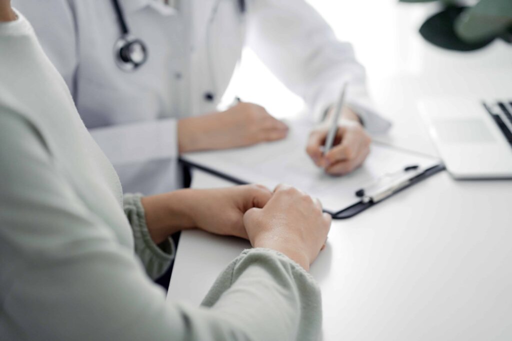 Patient consulting with doctor taking notes during medical appointment in a healthcare office.