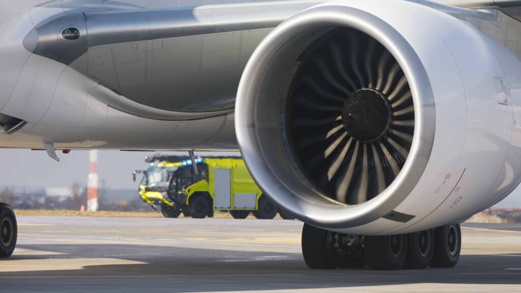 Close-up of airplane jet engine on airport runway with emergency response vehicle in the background.