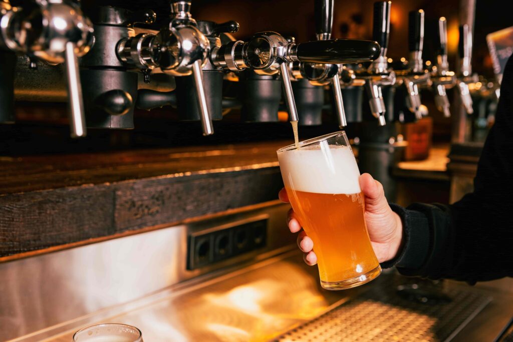 Bartender pouring draft beer from tap into glass at a bar.